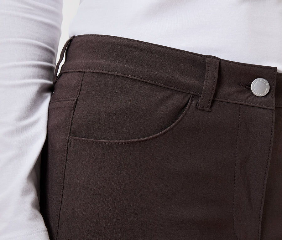 Nahaufnahme einer Frau, die ein langärmliges Oberteil und eine braune Hose mit Knopf trägt.