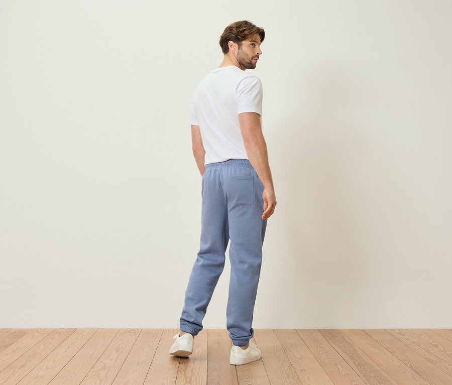 Mann in hellblauer Jogginghose und weißem T-Shirt, von hinten gesehen.