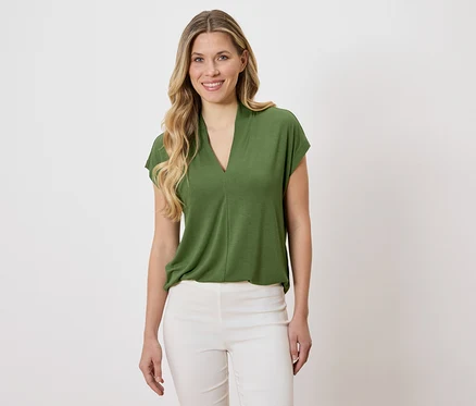 Frau trägt eine grüne Bluse und weiße Hose.