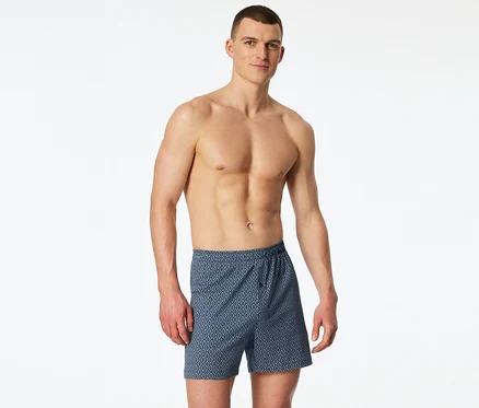 Ein oberkörperfreier Mann trägt blaue SCHIESSER Jersey-Boxer mit Rautenmuster.