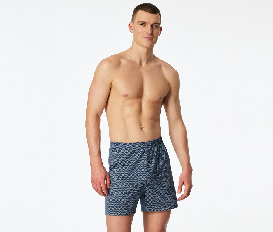 Mann mit freiem Oberkörper und blauen Boxershorts mit geometrischem Muster.