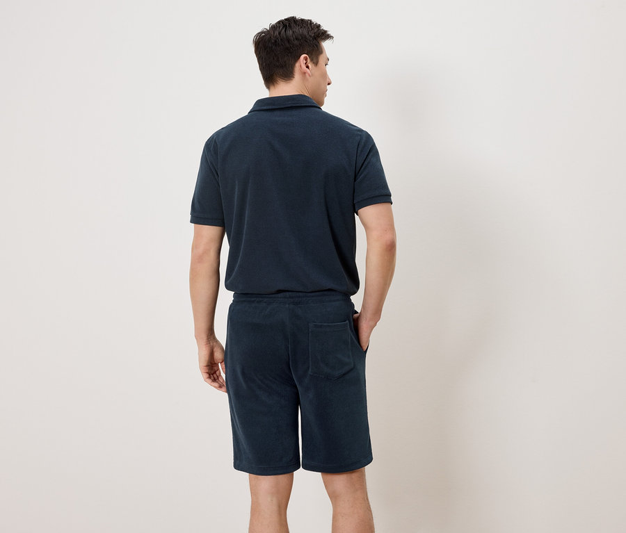 Ein Mann von hinten, der ein marineblaues Polohemd und Shorts trägt.