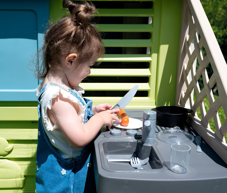 Mädchen schneidet Wurst in der Küche des Smoby Life Spielhauses »Pretty«.