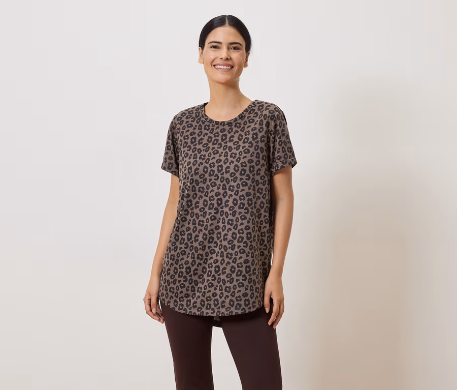 Eine Frau mit hochgesteckten Haaren trägt ein braunes Leopardenmuster-T-Shirt und braune Leggings vor einem hellen Hintergrund.