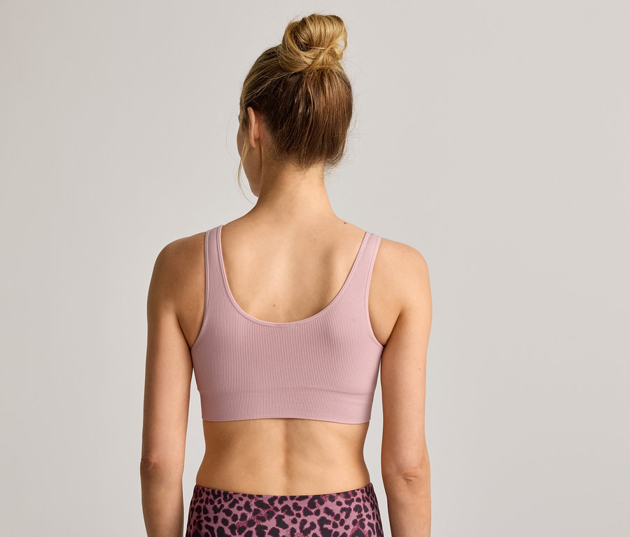 Rückansicht einer Frau mit Duttfrisur, die einen gerippten Sport-BH und Leggings mit Leopardenmuster trägt.
