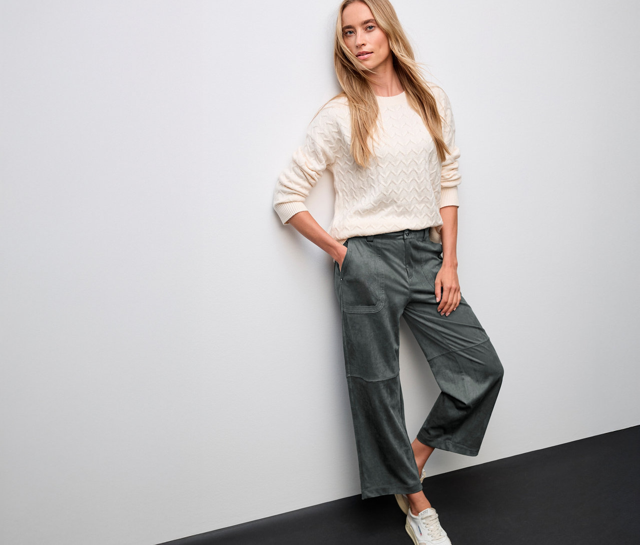 Frau posiert in cremefarbenem Pullover und grüner Street One Velourshose Straight Leg an einer Wand.