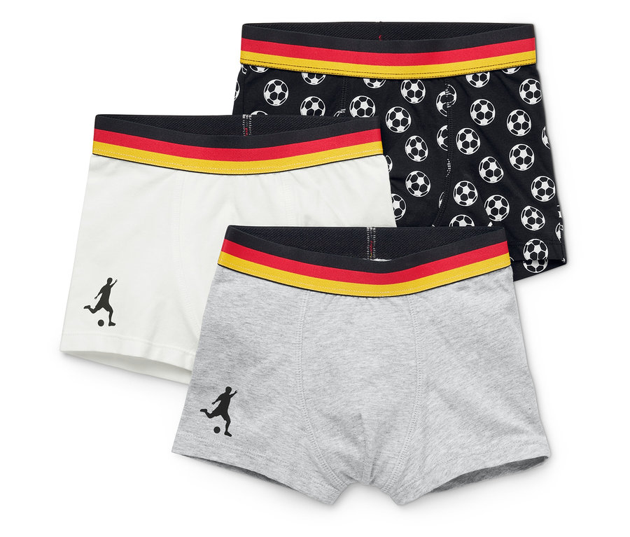 Drei Boxershorts liegen übereinander: eine graue, eine weiße mit Fußballspieler-Silhouette und eine schwarze mit Fußballmuster. Alle haben einen Bund in den deutschen Nationalfarben.