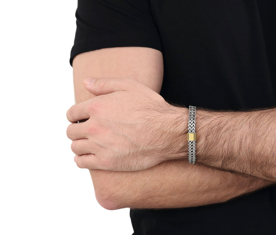 Nahaufnahme eines Mannes mit verschränkten Armen, der ein silbernes Gliederarmband mit goldenem Verschluss trägt.
