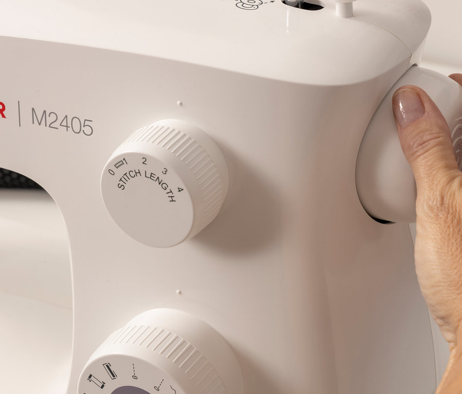 Hand verstellt den Drehknopf der Singer Nähmaschine »M2405« zur Einstellung der Stichlänge.