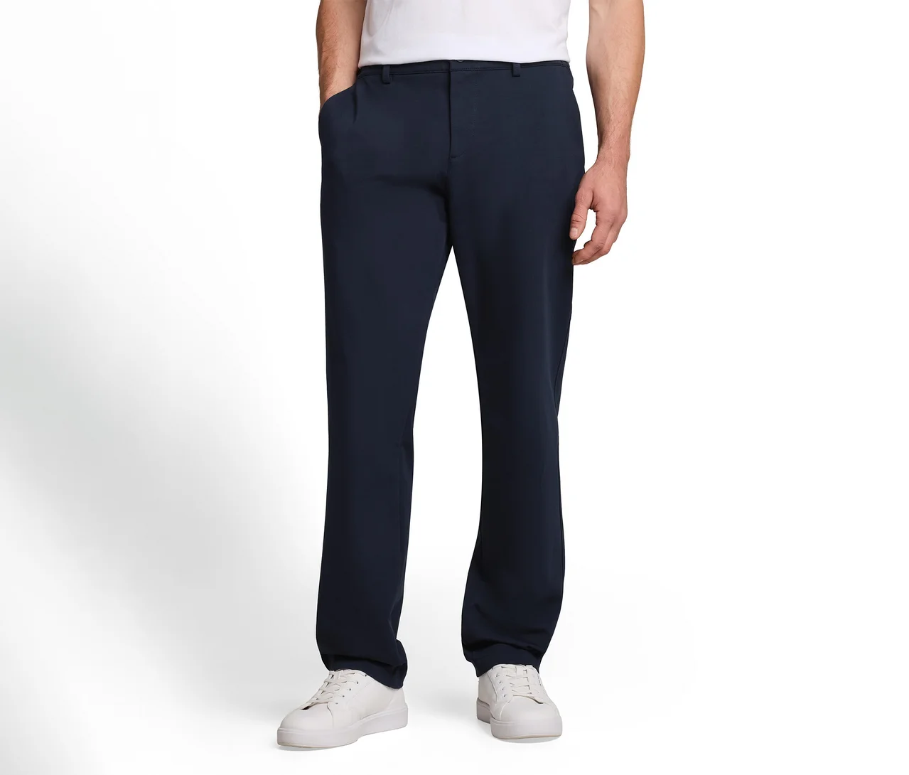 Mann in dunkelblauer Hose und weißen Sneakern, eine Hand in der Hosentasche.