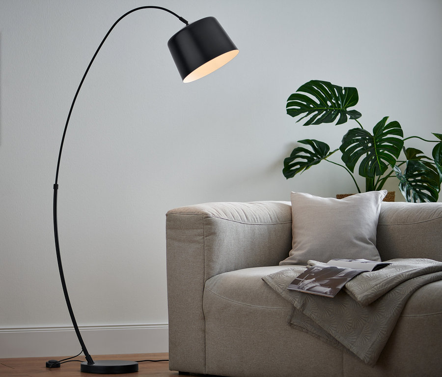 Eine schwarze Stehleuchte aus Metall steht neben einem Sofa.