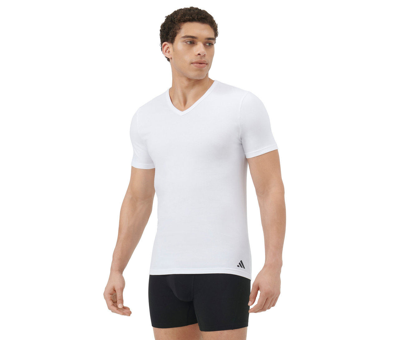 Mann in einem weißen V-Ausschnitt-T-Shirt und schwarzen Boxershorts, steht und blickt nach rechts vor weißem Hintergrund.