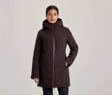 Frau mit zurückgebundenem dunklem Haar, die nach vorne blickt und eine dunkelbraune Kapuzenjacke mit den Händen in den Taschen trägt.