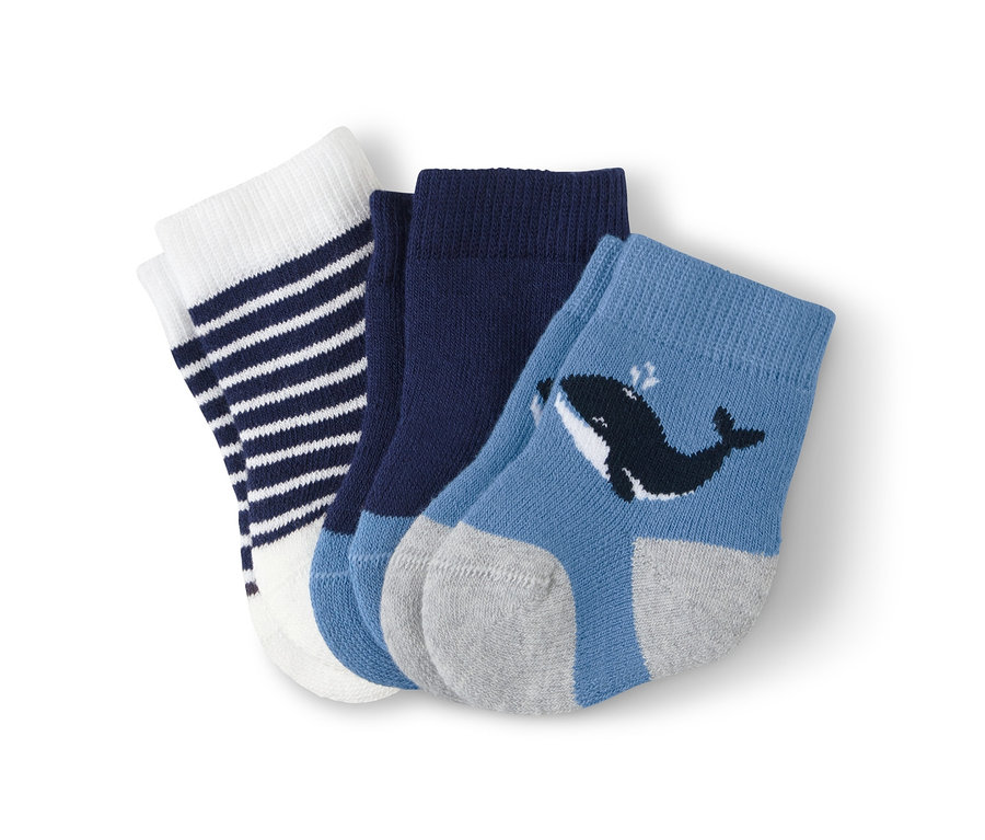 Drei Paar Babysocken: ein Paar weiß mit dunkelblauen Streifen, ein Paar dunkelblau und ein Paar hellblau mit grauer Ferse und Walbild.