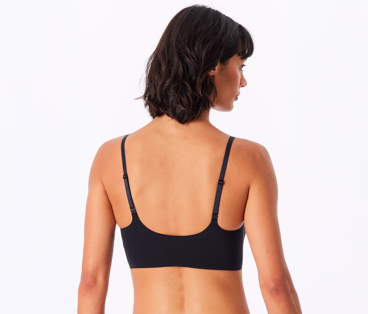 Eine Frau mit kurzen dunklen Haaren ist von hinten zu sehen und blickt über ihre rechte Schulter. Sie trägt ein schwarzes SCHIESSER Invisible Bustier mit Pads.