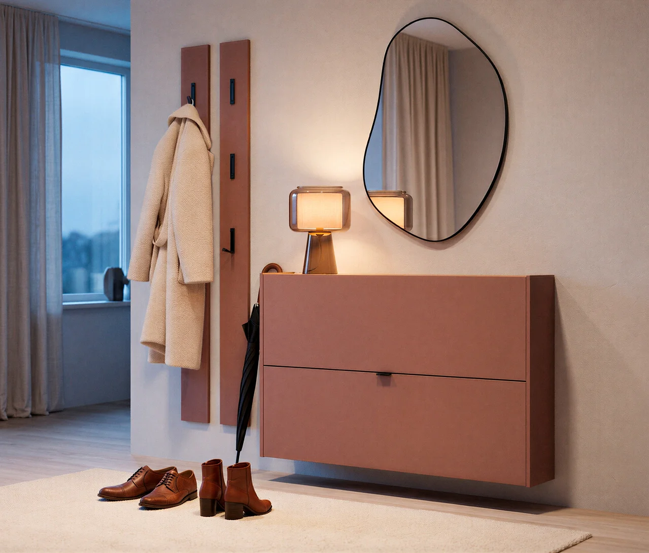 Ein moderner Eingangsbereich mit einem staubrosa Wand-Schuhschrank, darauf eine Tischlampe und darüber ein unregelmäßig geformter WOOOD Spiegel »Romee«. Links hängt ein heller Mantel an einer passenden rosa Garderobe, daneben lehnt ein schwarzer Regenschirm. Braune Herrenschuhe und Damen-Stiefeletten stehen auf einem hellen Teppich am Boden.