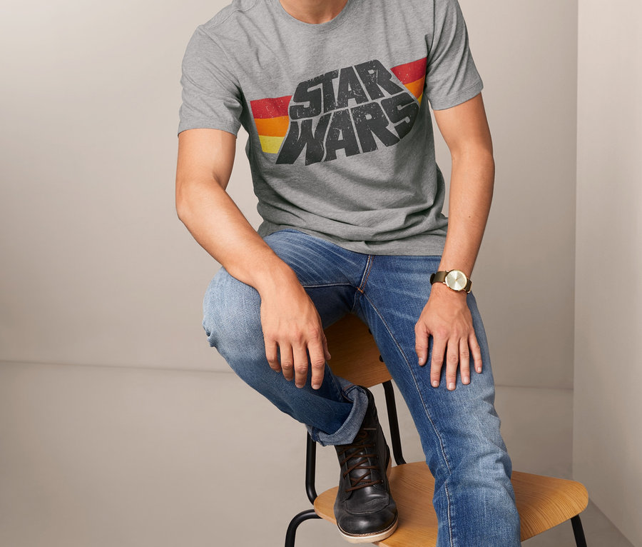 Mann sitzt auf einem Stuhl und trägt ein graues T-Shirt mit dem Aufdruck Star Wars.