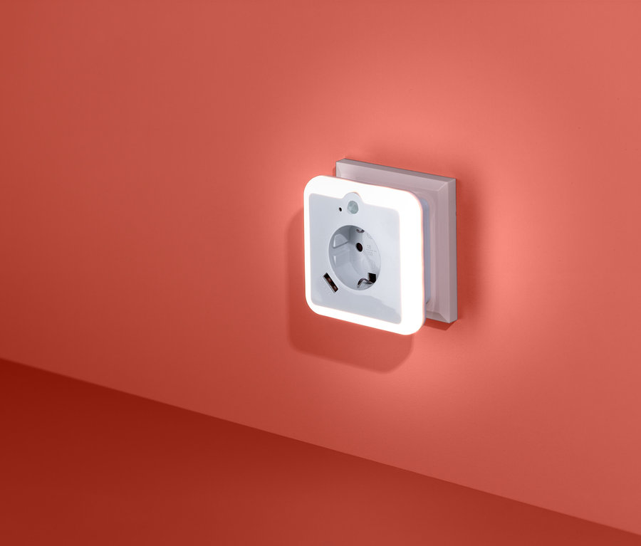 An einer korallenroten Wand befindet sich eine Steckdose mit einem LED-Nachtlicht mit USB-Lademöglichkeit.