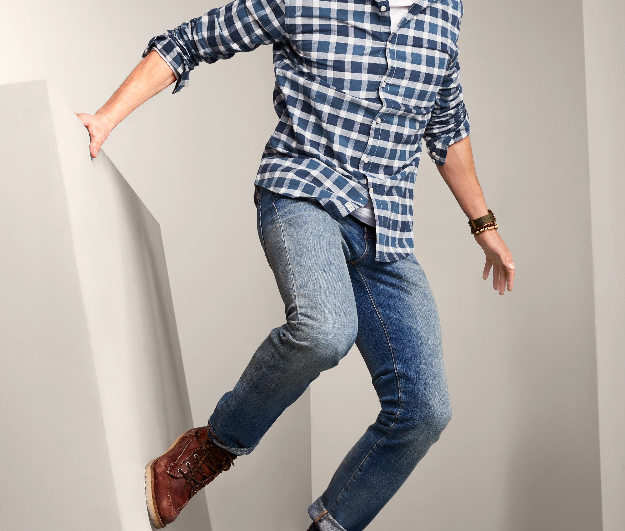 Mann mit Bart springt, trägt ein Flanell-Hemd, Jeans und braune Stiefel.