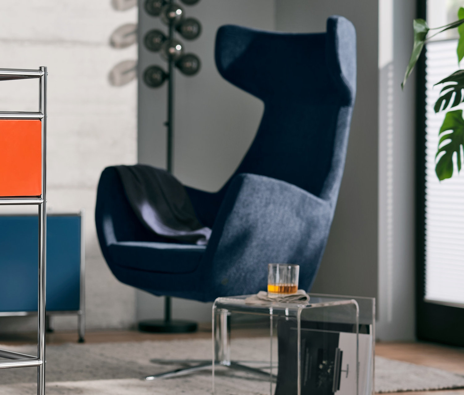 Ein Barwagen Metall »CN3« mit Schublade, orange. Im Hintergrund ein blauer Ohrensessel »Claire«.