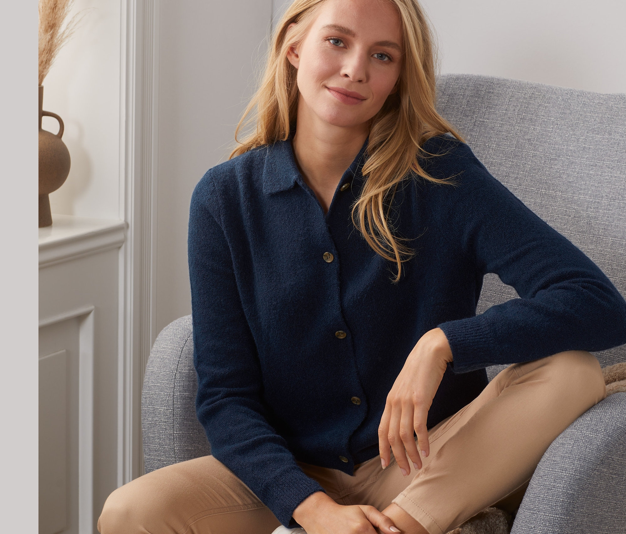 Frau sitzt im Sessel und trägt einen dunkelblauen Cardigan mit Kragen.