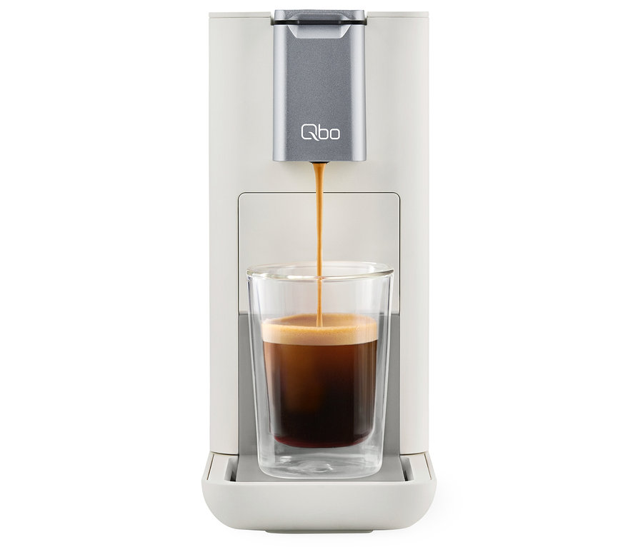 Kaffee läuft aus der Qbo ESSENTIAL Bright Sand Kaffeemaschine in ein Glas.