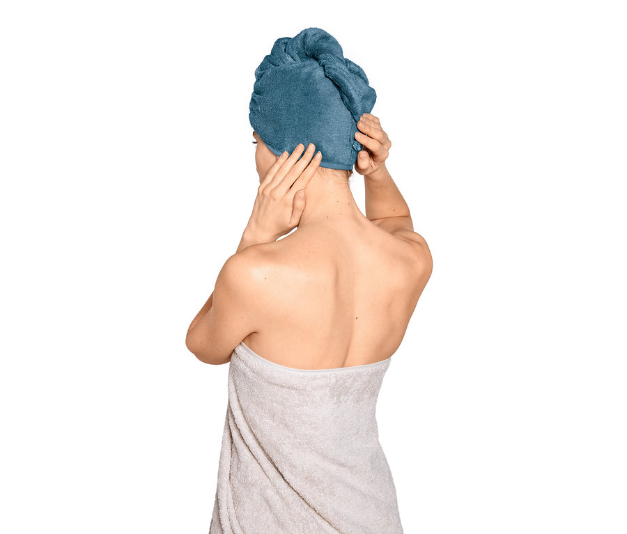 Frau befestigt blaues Turban-Handtuch auf dem Kopf.