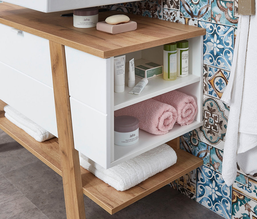 Weißer Waschbecken-Unterschrank »Novolino« mit Holzplatte und offenen Regalen mit Kosmetika und Handtüchern.