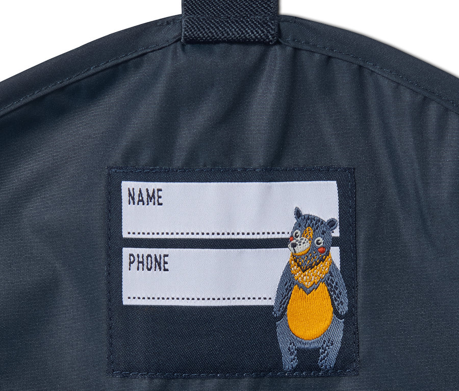 Detail einer dunkelblauen Regenhose mit Namensschild und Bärenbild.