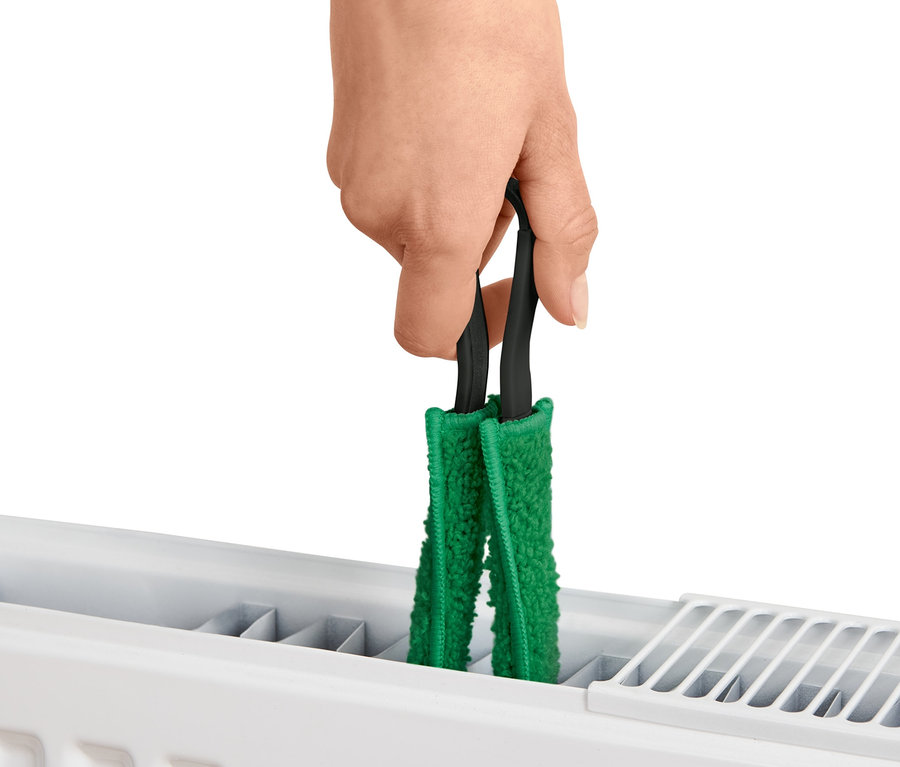 Eine Hand hält eine Pflanzenbürste an einem Heizkörper.