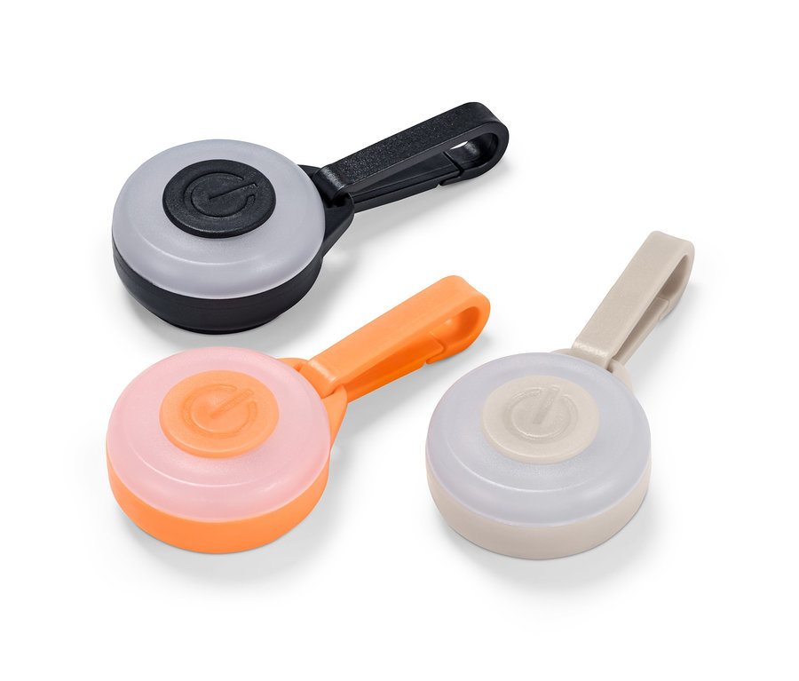 Drei LED-Anhänger liegen auf einer weißen Oberfläche. Einer ist schwarz, einer orange und einer beige.