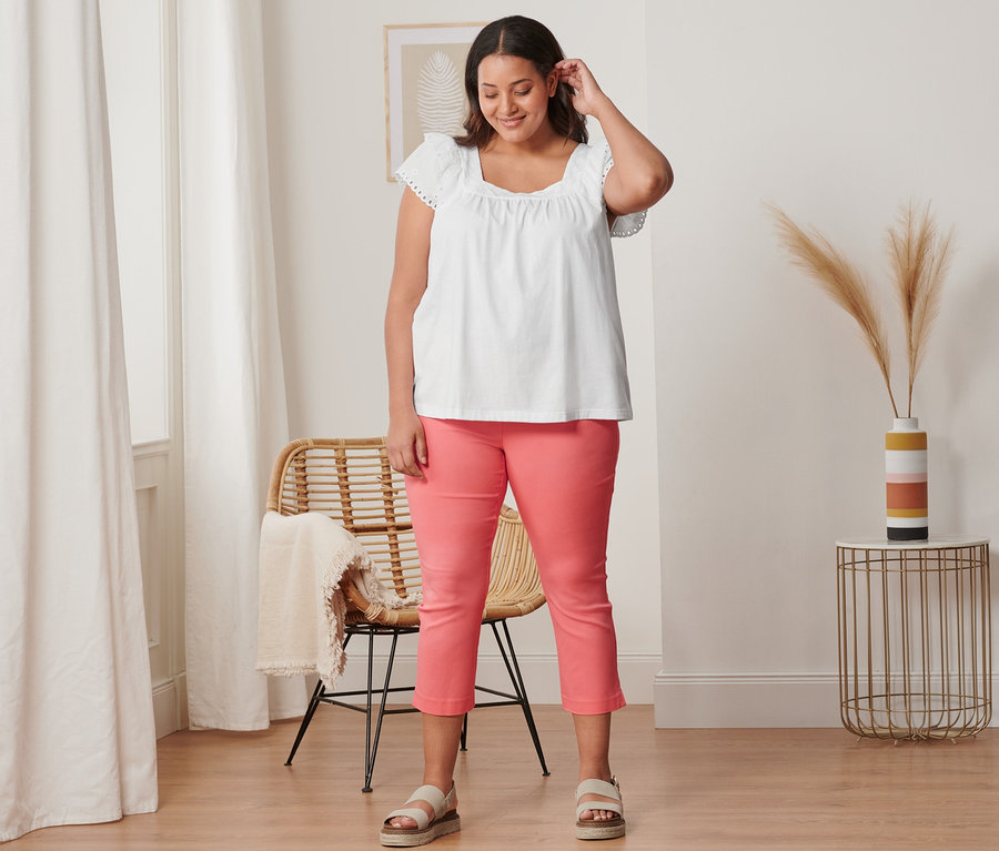 Frau trägt eine koralle 7/8-Stretchhose, ein weißes Shirt mit Stickerei und Plateau-Sandale aus Leder.