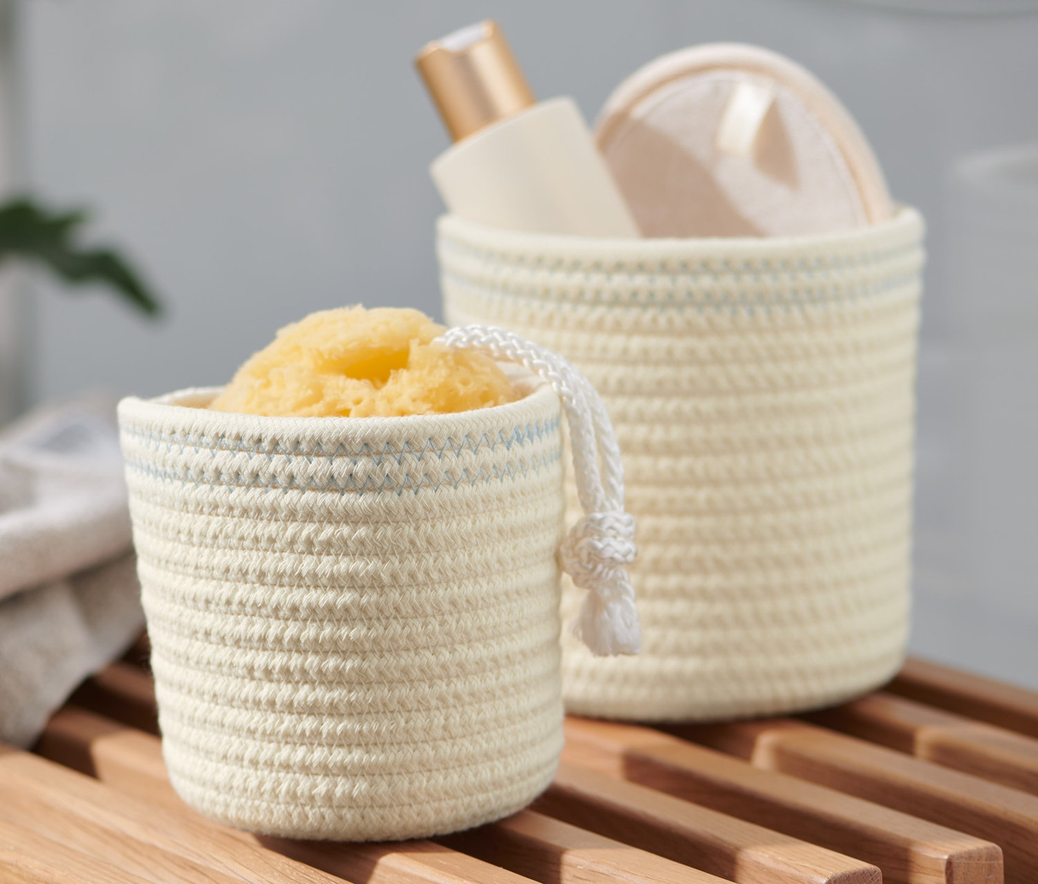 Zwei crèmeweiß-blaue Aufbewahrungskörbe auf einem Holzregal, einer mit einem Schwamm, der andere mit einer Flasche.