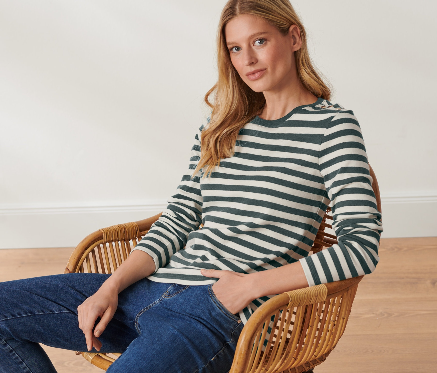 Frau sitzt im Sessel und trägt ein gestreiftes Langarmshirt.