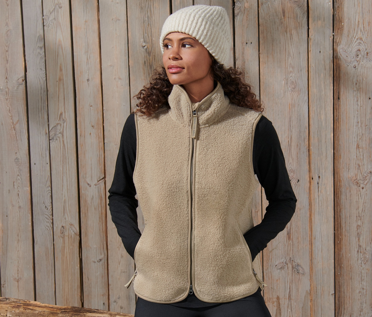 Frau posiert in Teddy-Weste und Wollmütze.