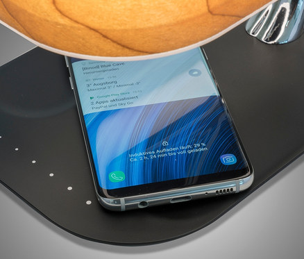 Handy wird auf einer Induktiv-Ladestation mit BT-Lautsprecher und Lampe geladen.