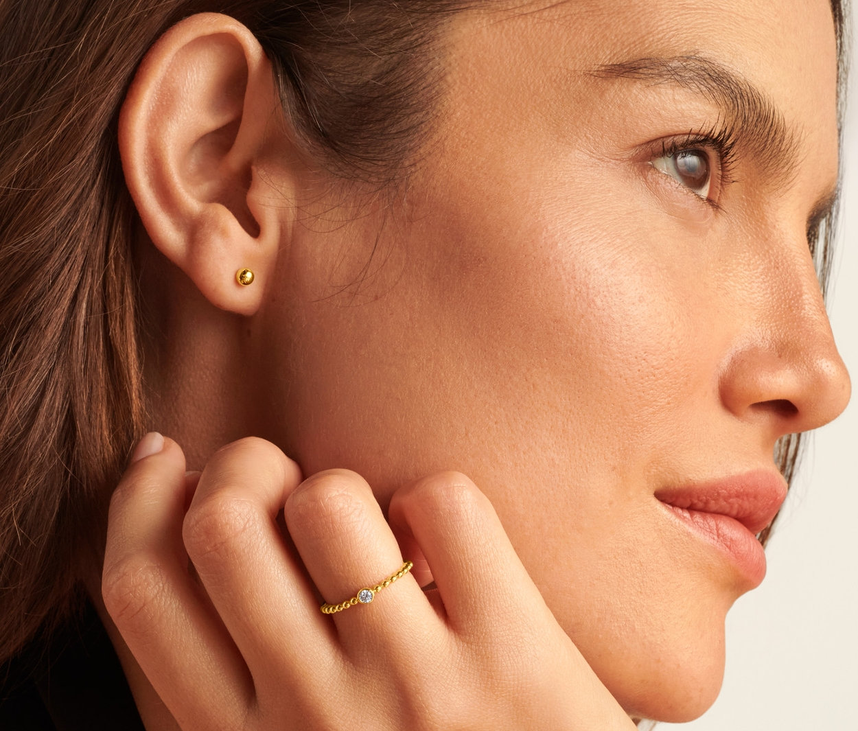 Detailaufnahme einer Frau mit Finger auf der Wange, die einen 585 Gold Ring mit Kugeln und Zirkonia und 585 Gold Ohrstecker Kugel trägt.