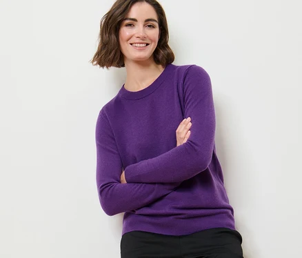 Frau posiert mit verschränkten Armen in einem lila Feinstrickpullover mit Cashmere und einer schwarzen Hose.