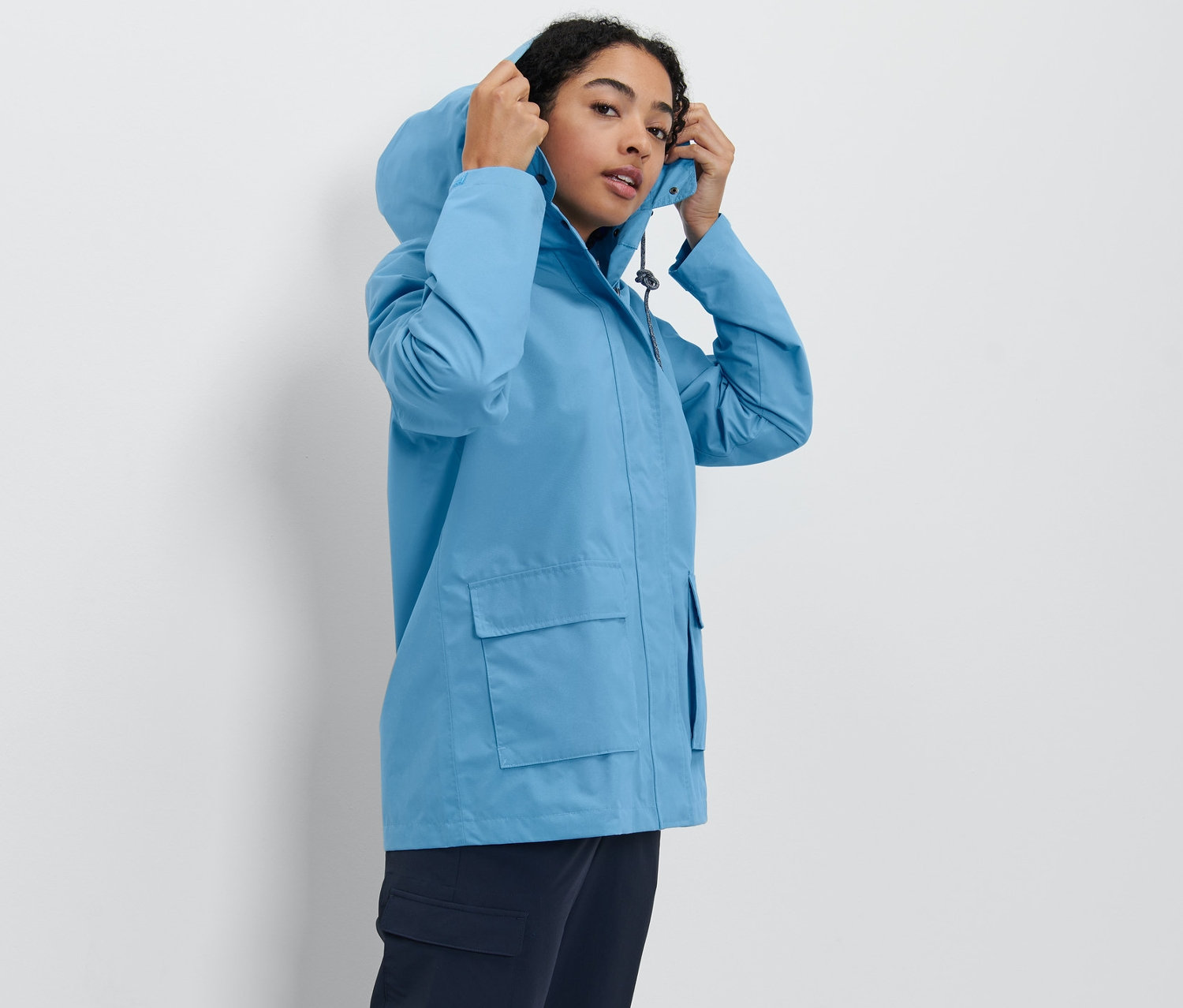 Frau setzt die Kapuze ihrer Allwetterjacke auf.