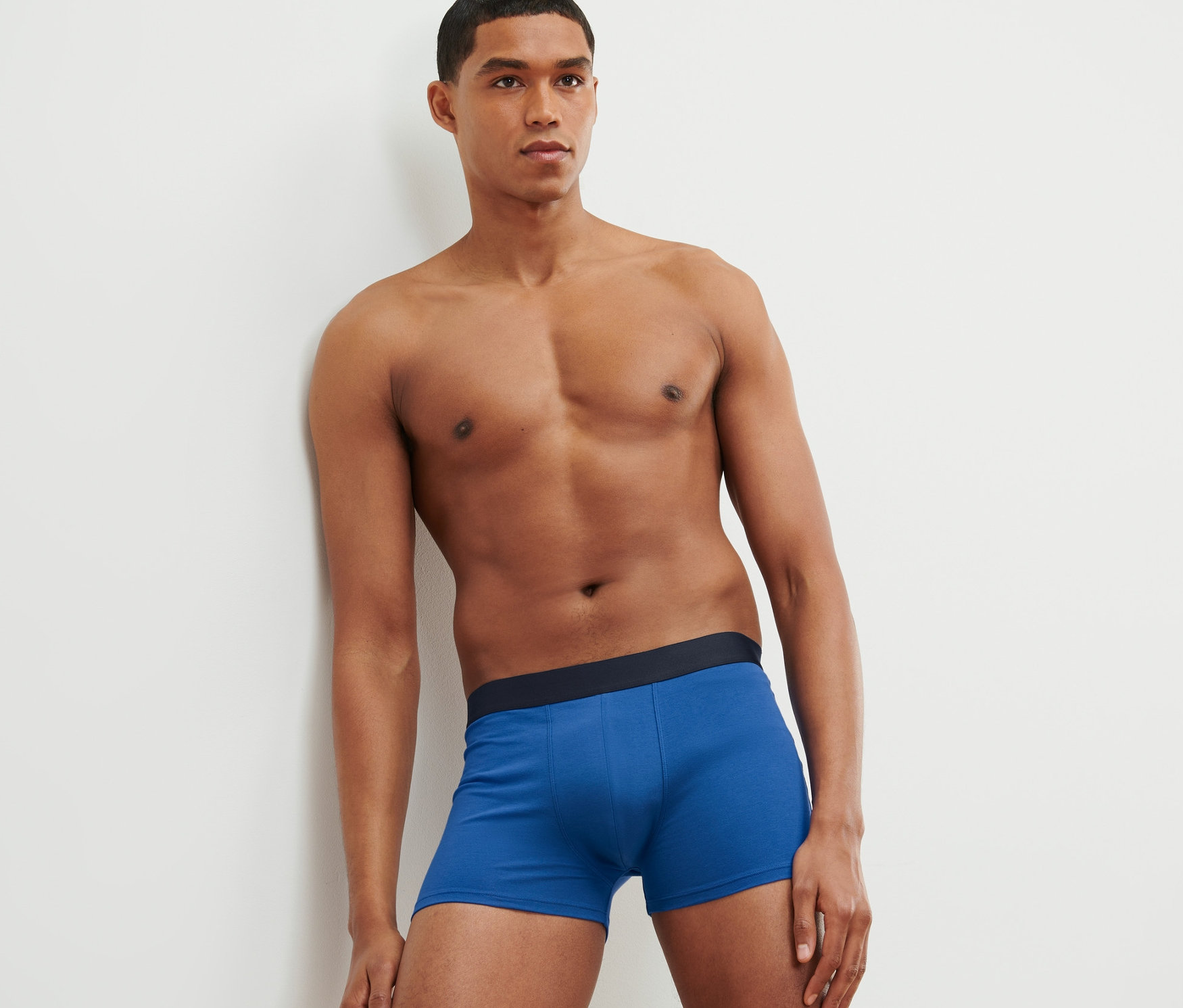 Mann lehnt an Wand und trägt 4 Slipboxer, blau, Alloverprint und grau.