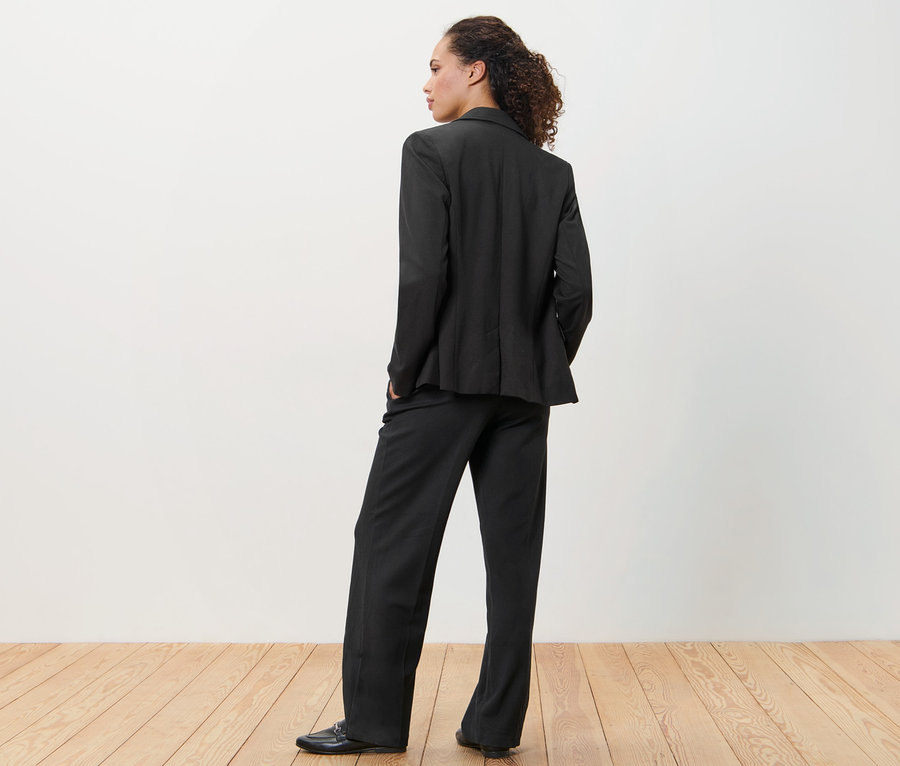 Frau in schwarzem Jerseyblazer und Hose steht mit dem Rücken zur Kamera.