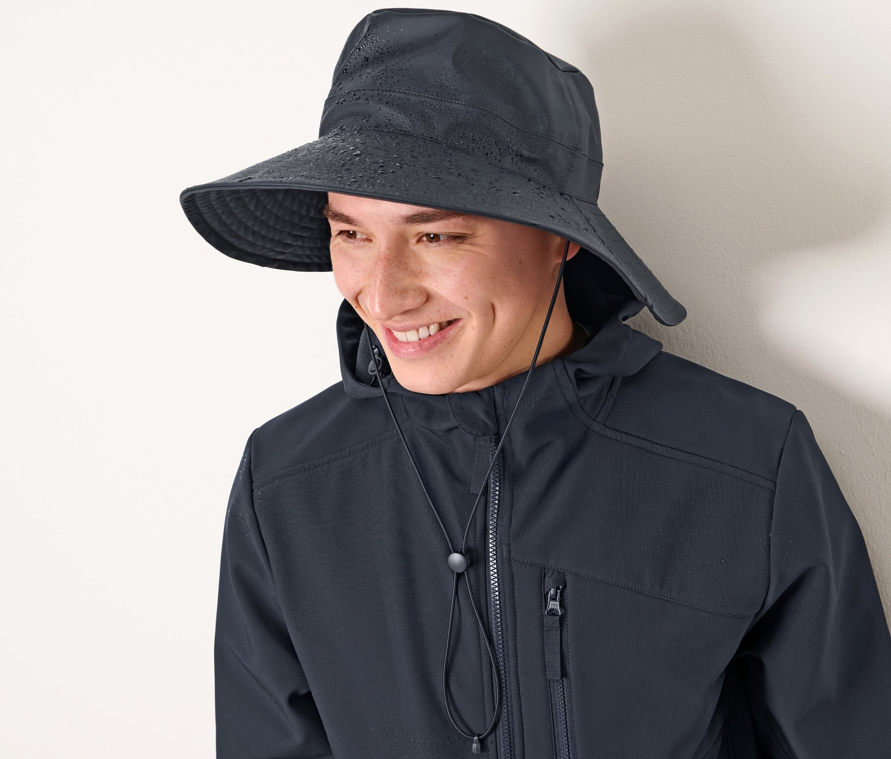 Mann lächelt und trägt einen dunkelblauen Regenhut und eine Jacke.