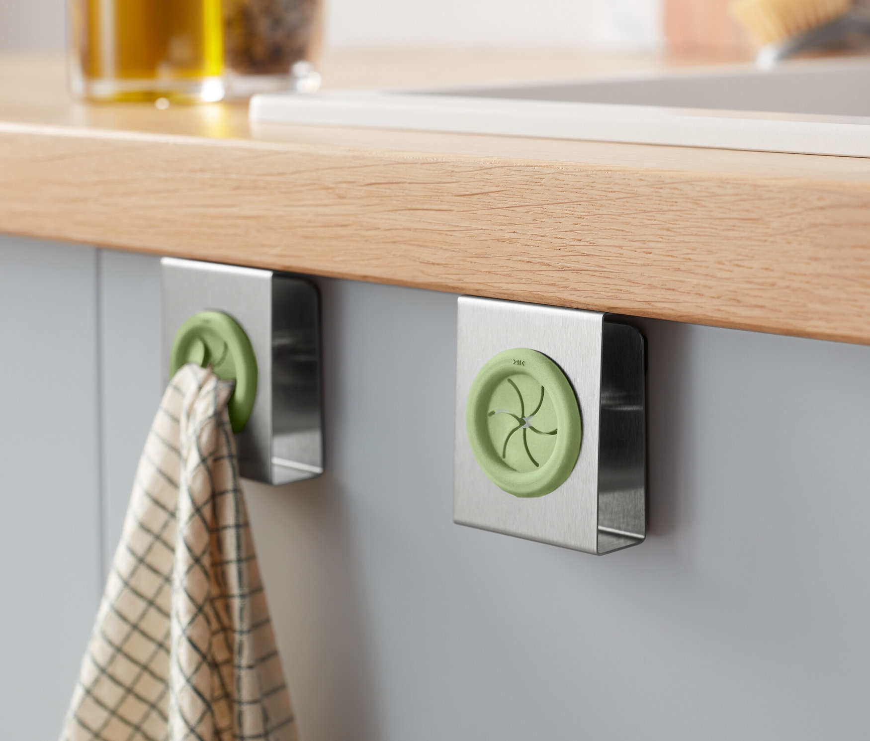 Zwei Geschirrtuchhalter sind an einem Schrank befestigt, an einem hängt ein Geschirrtuch.