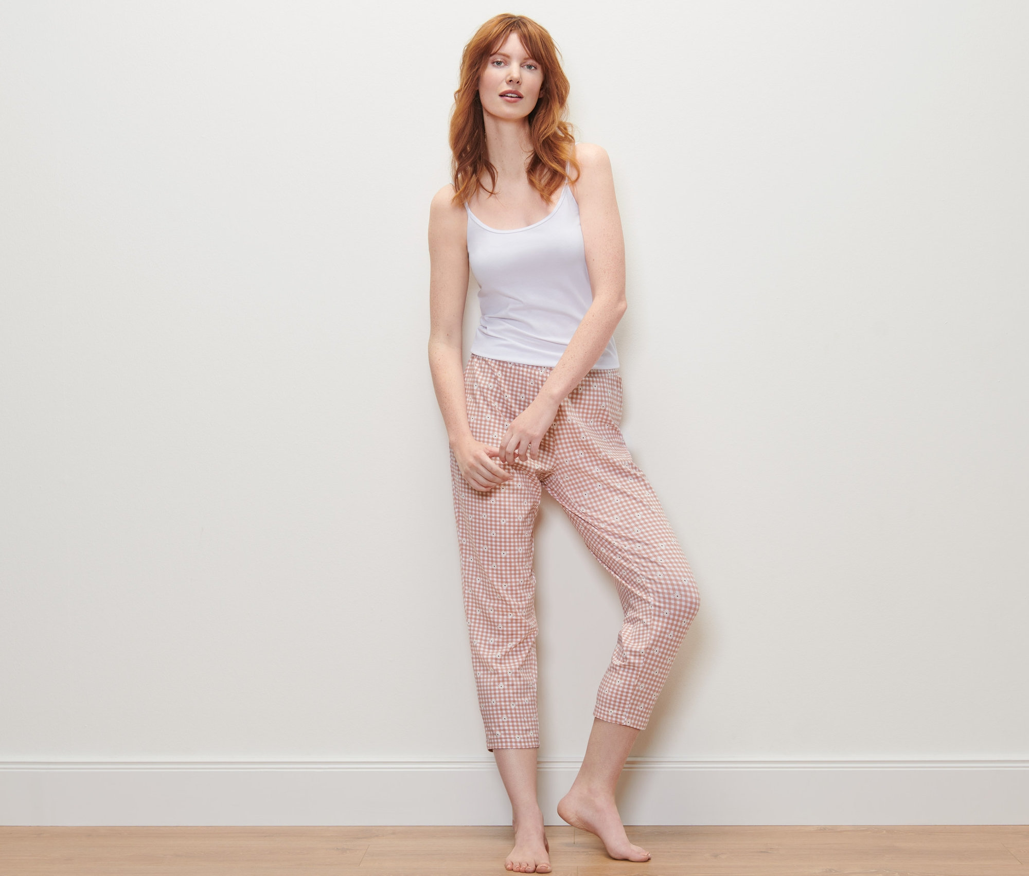 Rothaarige Frau steht und trägt ein weisses Top und eine karierte 7/8-Pyjamahose.