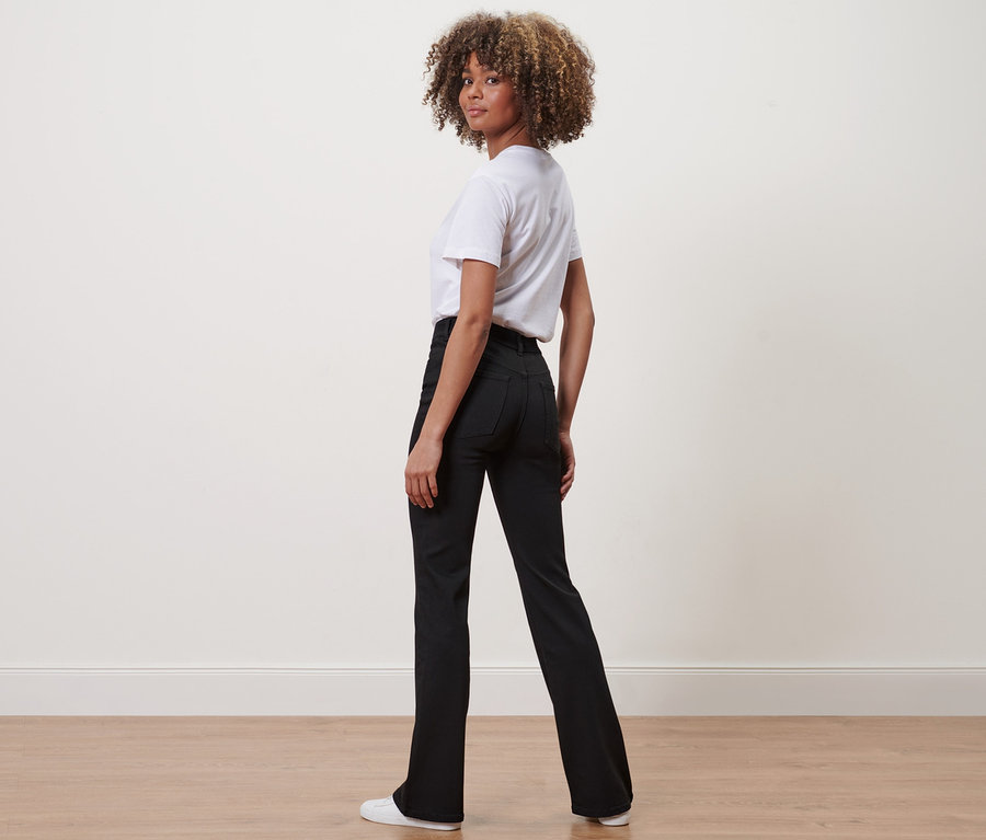 Frau blickt über die Schulter und trägt eine schwarze Bootcut Denim – Fit Jola und ein weißes T-Shirt.