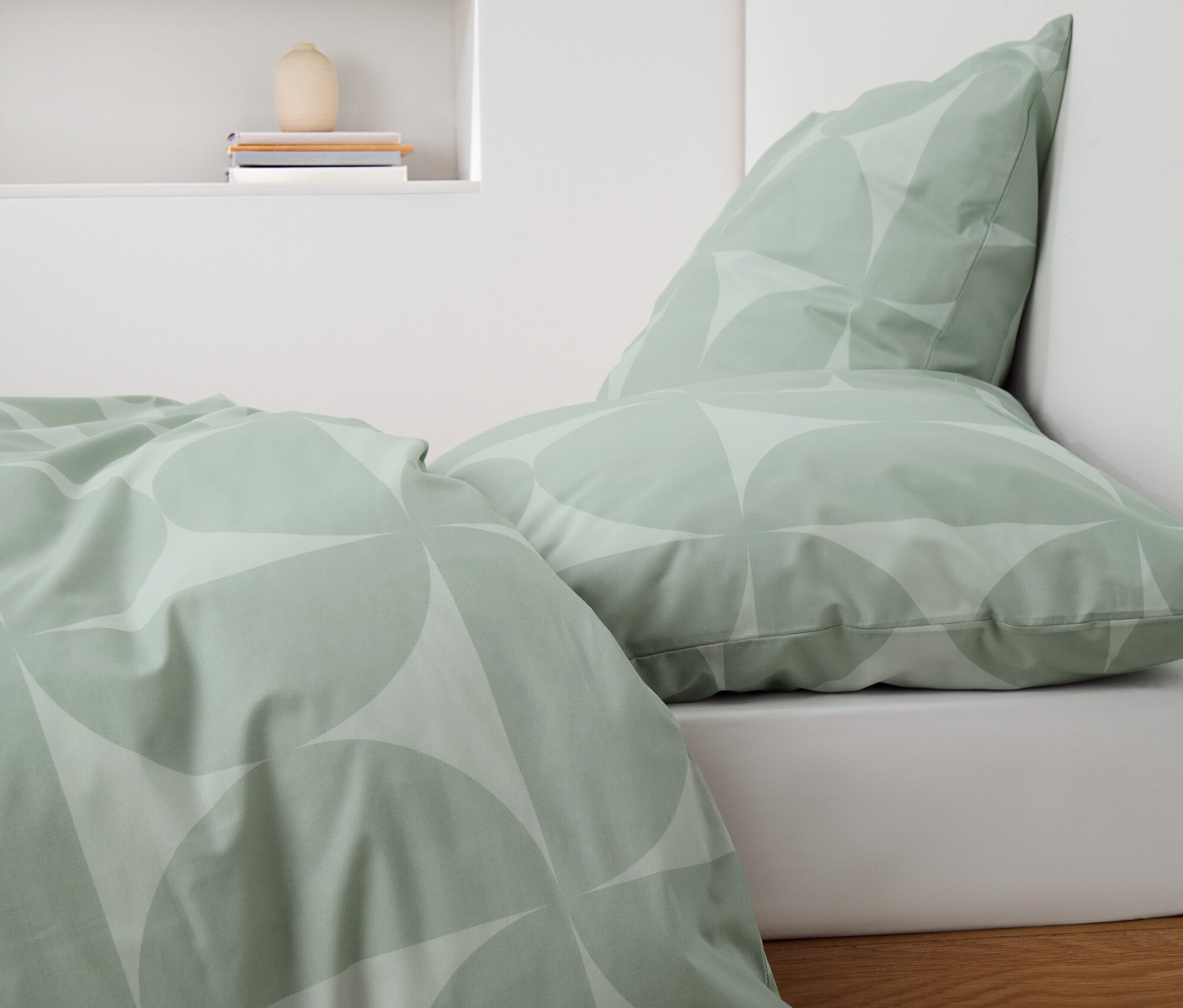 Grüne Renforcé-Bettwäsche mit geometrischem Muster auf einem Bett.