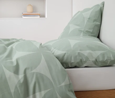 Grüne Renforcé-Bettwäsche mit geometrischem Muster auf einem Bett.
