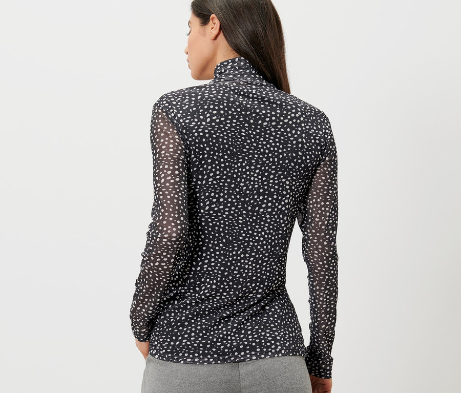 Rückansicht einer Frau mit dunklen Haaren in einem gepunkteten Mesh-Rollkragenshirt.