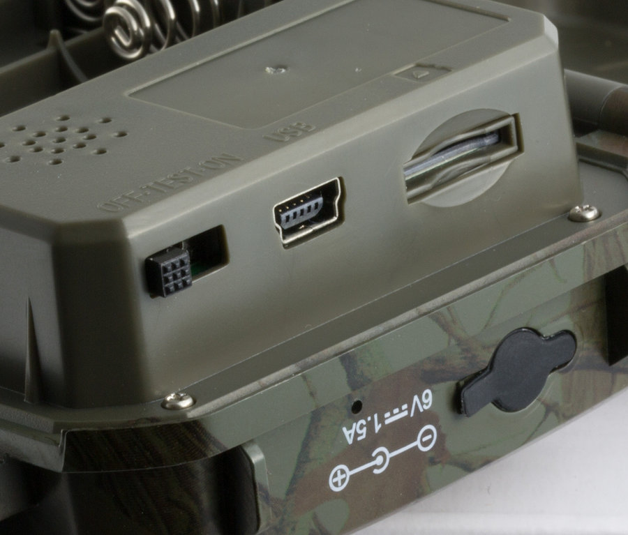 Detailaufnahme einer graugrünen Wildkamera mit USB-Anschlüssen und SD-Kartensteckplatz.