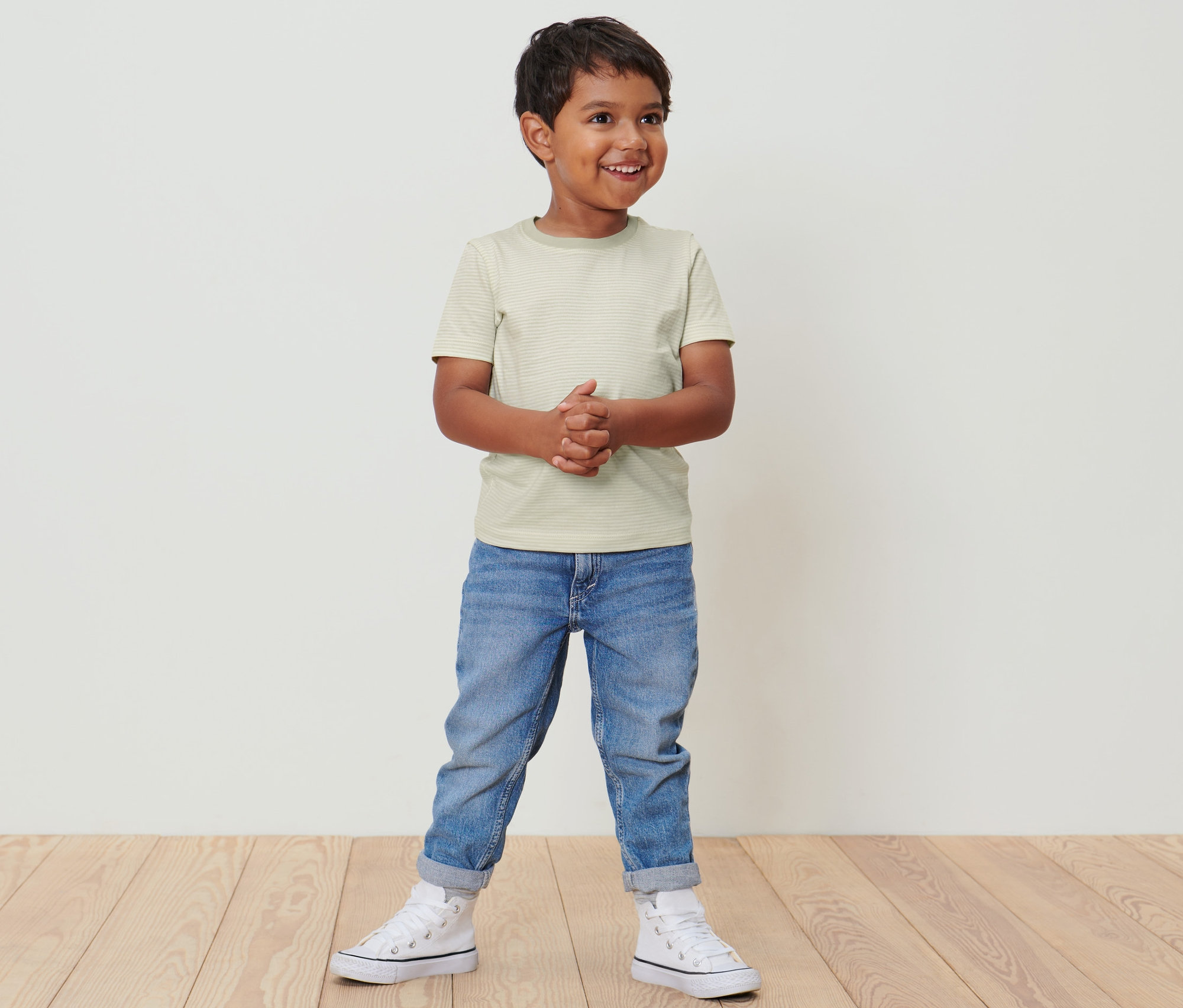 Ein Junge steht und trägt 2 Kinder-T-Shirts, Jeans und Turnschuhe.